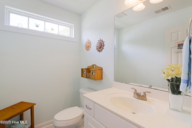 half bathroom with vanity, toilet, baseboards, and visible vents
