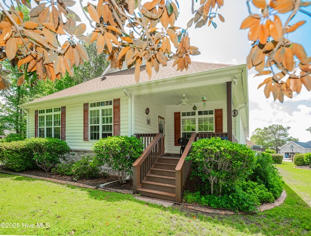 view of front facade with a porch, roof with shingles, a front lawn, and a ceiling fan