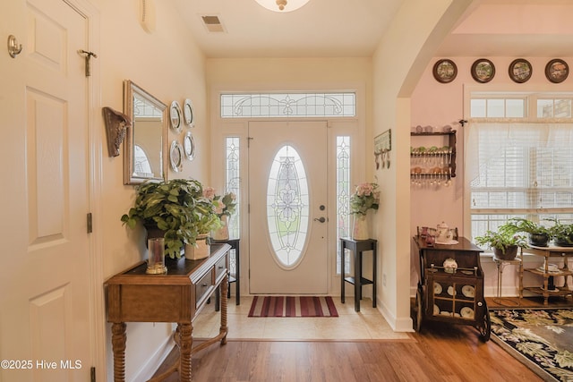 foyer with arched walkways, baseboards, visible vents, and wood finished floors