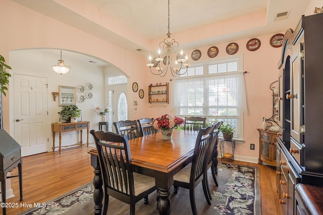 dining space featuring an inviting chandelier, visible vents, wood finished floors, arched walkways, and a raised ceiling