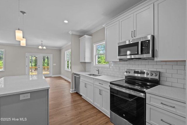 kitchen with stainless steel appliances, ornamental molding, light wood finished floors, backsplash, and white cabinets