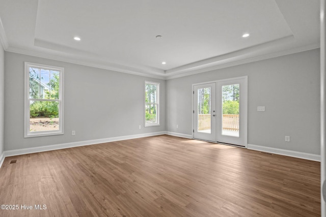 empty room with a raised ceiling, wood finished floors, recessed lighting, french doors, and crown molding