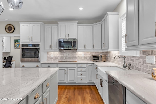 kitchen with backsplash, appliances with stainless steel finishes, a sink, light stone counters, and white cabinetry