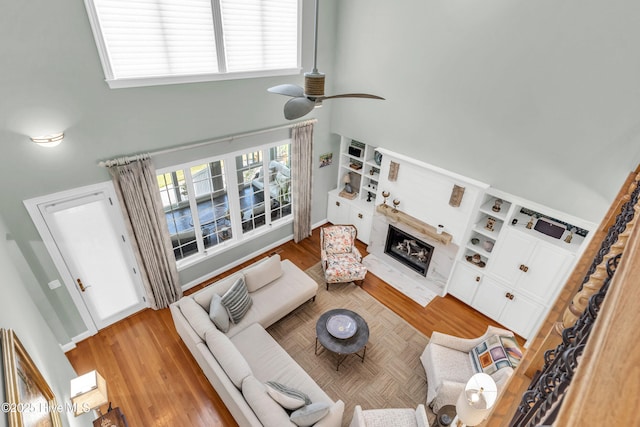 living room featuring a glass covered fireplace, a ceiling fan, and a towering ceiling