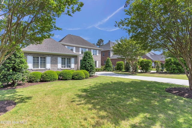 colonial inspired home with brick siding, a front yard, and roof with shingles