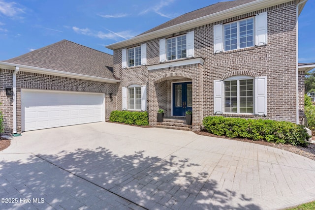 colonial house with brick siding, an attached garage, and driveway