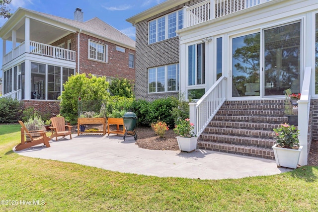 rear view of house featuring a yard, brick siding, a patio area, and a balcony