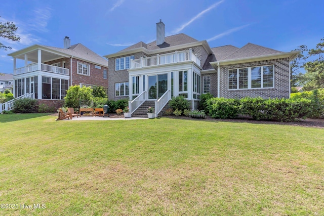 rear view of house featuring a chimney, a balcony, a yard, brick siding, and a patio area