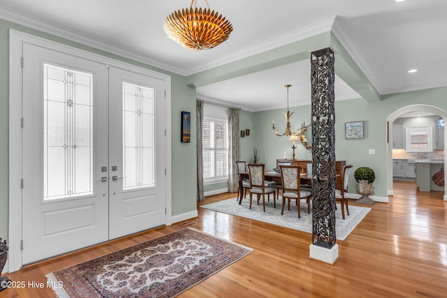 foyer entrance with an inviting chandelier, baseboards, french doors, arched walkways, and light wood finished floors