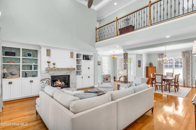 living area with crown molding, light wood-style floors, a premium fireplace, and a notable chandelier