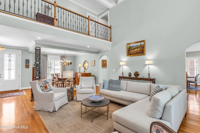 living room featuring arched walkways, wood finished floors, a chandelier, and ornamental molding