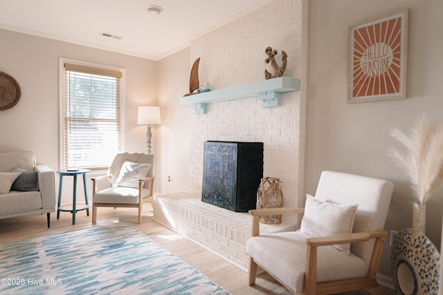 living area with wood finished floors, ornamental molding, and a brick fireplace