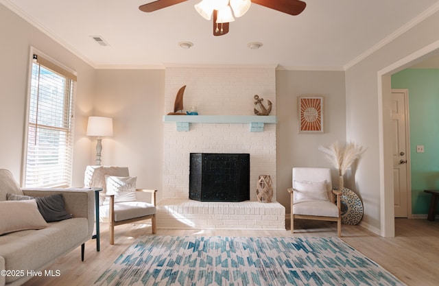living area with a ceiling fan, wood finished floors, ornamental molding, a brick fireplace, and baseboards