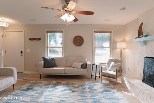 living room featuring healthy amount of natural light, ornamental molding, light wood-style floors, ceiling fan, and a fireplace