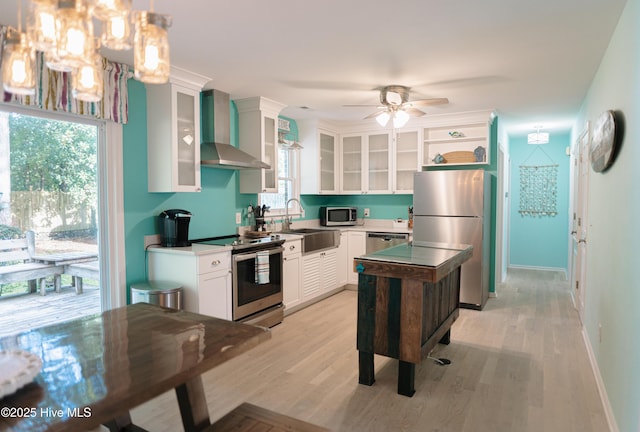 kitchen featuring appliances with stainless steel finishes, wall chimney exhaust hood, a sink, light wood-style floors, and white cabinetry