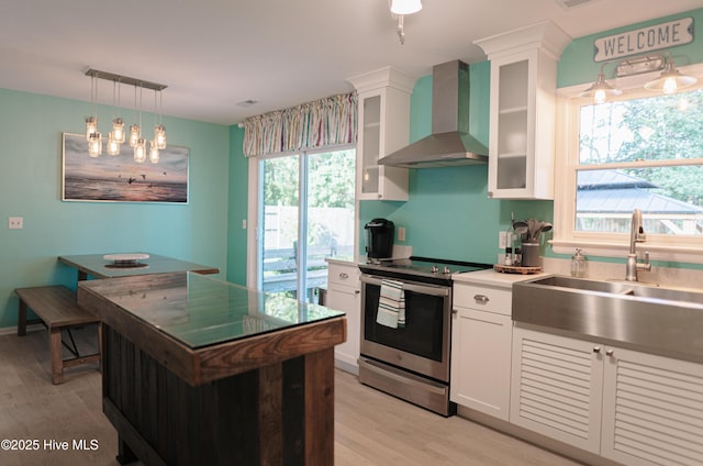 kitchen with wall chimney range hood, stainless steel electric range oven, light wood-style flooring, and a sink