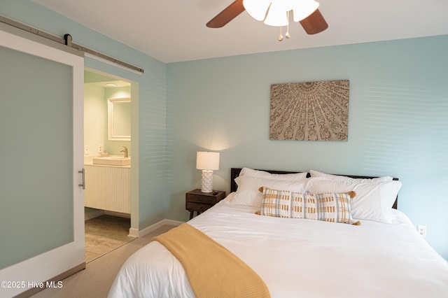 bedroom with a sink, a barn door, ensuite bathroom, a ceiling fan, and light colored carpet