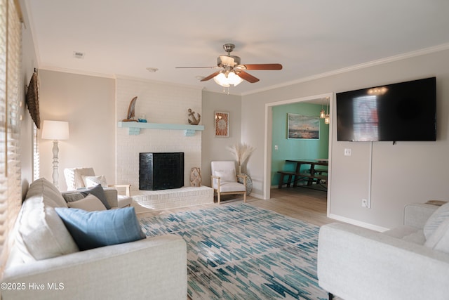 living area with a ceiling fan, ornamental molding, a brick fireplace, baseboards, and wood finished floors