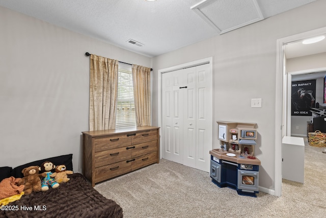 carpeted bedroom with a closet, attic access, a textured ceiling, and visible vents