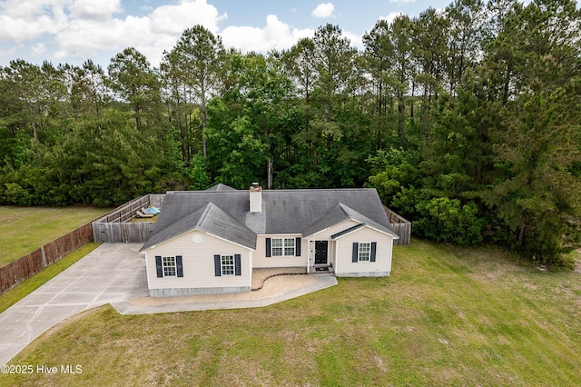 view of front facade featuring concrete driveway, fence, a chimney, and a front yard