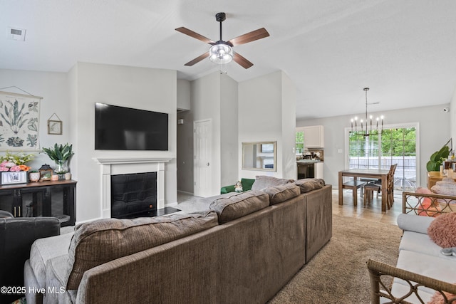 living room featuring a glass covered fireplace, ceiling fan with notable chandelier, and visible vents