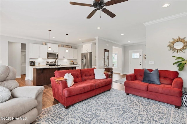 living area with light wood-style flooring, a ceiling fan, recessed lighting, crown molding, and baseboards