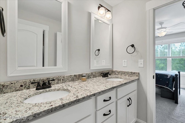 ensuite bathroom featuring double vanity, ceiling fan, and baseboards