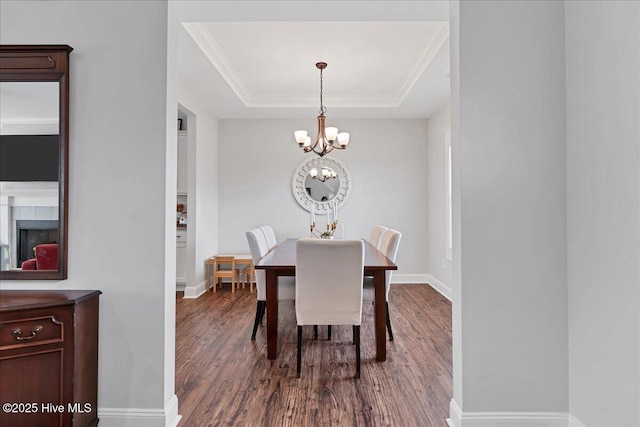dining area featuring a chandelier, dark wood-type flooring, a raised ceiling, baseboards, and a fireplace