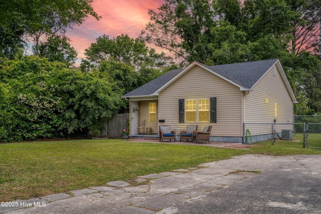 view of front of property with a gate, roof with shingles, fence, a front yard, and central AC unit