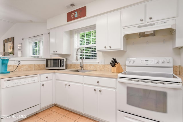 kitchen featuring plenty of natural light, under cabinet range hood, white appliances, visible vents, and a sink