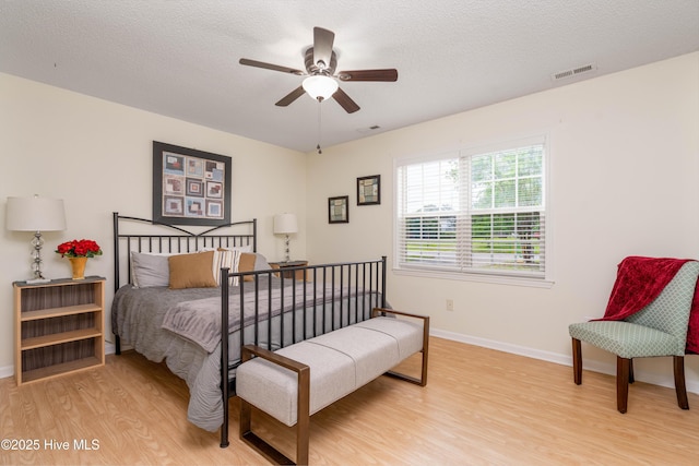 bedroom featuring light wood-style floors, visible vents, baseboards, and a textured ceiling