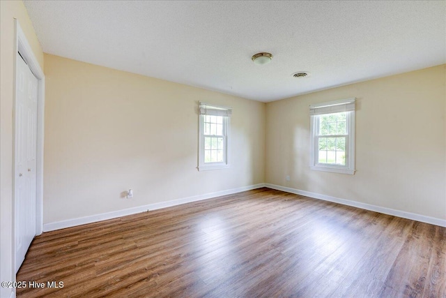 unfurnished bedroom with multiple windows, wood finished floors, baseboards, and a textured ceiling