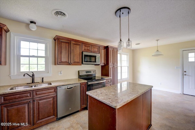 kitchen featuring appliances with stainless steel finishes, a sink, a textured ceiling, decorative light fixtures, and a kitchen island