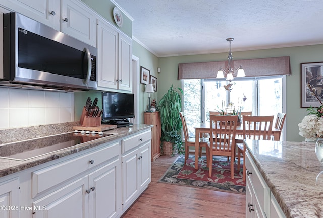 1 Collett Ln, Pinehurst, NC 28374 - kitchen featuring stainless steel microwave, black electric stovetop, light wood-style floors, white cabinetry, and backsplash
