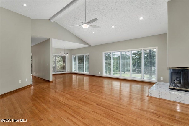 unfurnished living room featuring beamed ceiling, wood finished floors, healthy amount of natural light, ceiling fan, and high vaulted ceiling