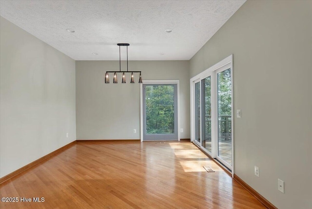 spare room with light wood-type flooring, a textured ceiling, a chandelier, and baseboards