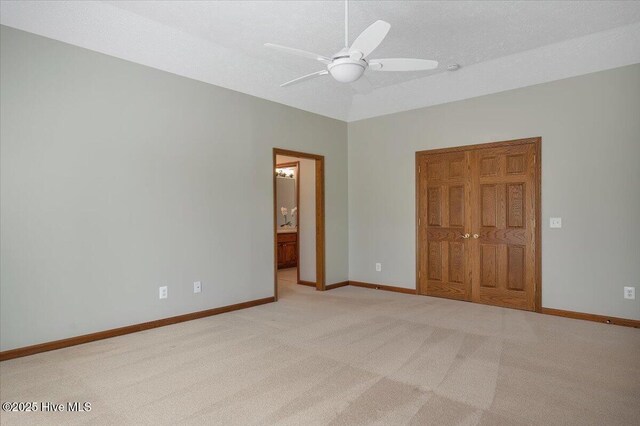 unfurnished bedroom with light carpet, baseboards, ensuite bath, and a ceiling fan