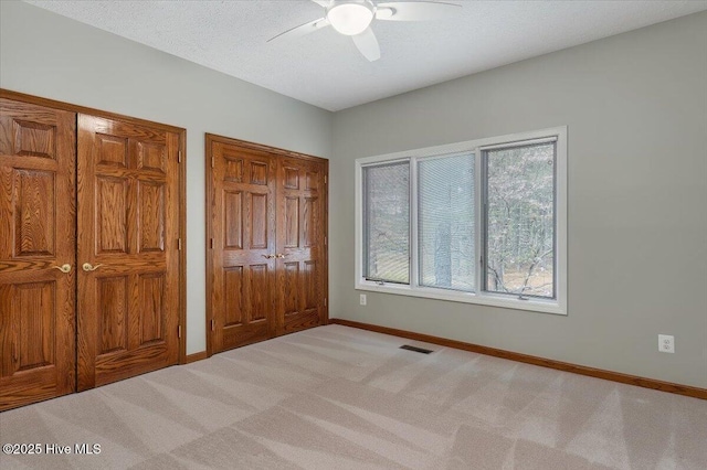 unfurnished bedroom featuring baseboards, light carpet, multiple closets, and ceiling fan