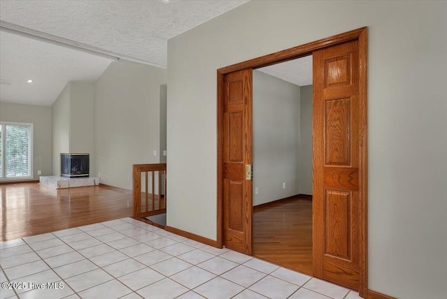 corridor featuring light wood finished floors, a textured ceiling, baseboards, and vaulted ceiling