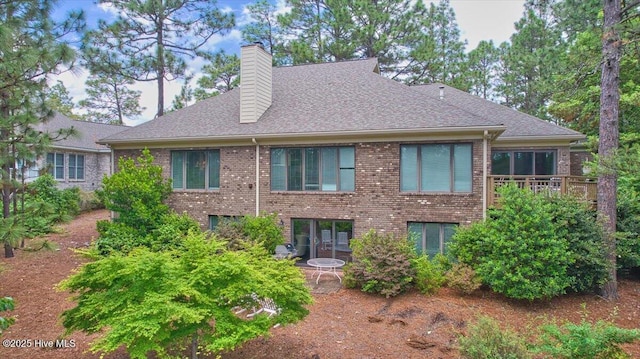 rear view of property featuring a chimney, brick siding, and roof with shingles