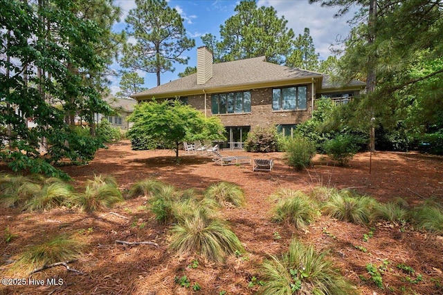 back of house featuring a chimney, brick siding, and a shingled roof