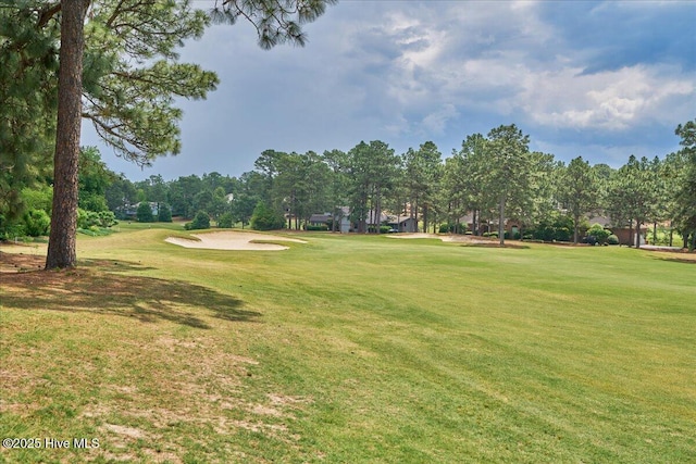 view of community with a lawn, golf course view, and view of wooded area