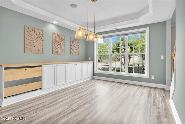 unfurnished dining area with a tray ceiling, light wood-style floors, and baseboards