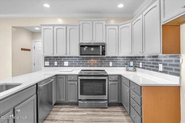 kitchen with stainless steel appliances, tasteful backsplash, ornamental molding, light wood-type flooring, and gray cabinetry