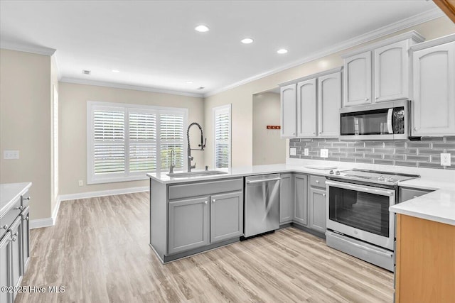 kitchen featuring a sink, a peninsula, gray cabinets, appliances with stainless steel finishes, and light wood-style floors