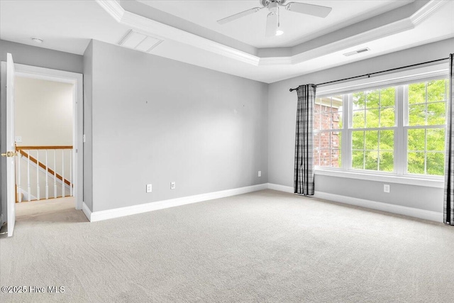 carpeted empty room with a tray ceiling, ceiling fan, baseboards, and visible vents