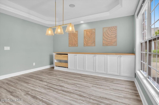 spare room with a tray ceiling, light wood-style floors, and baseboards