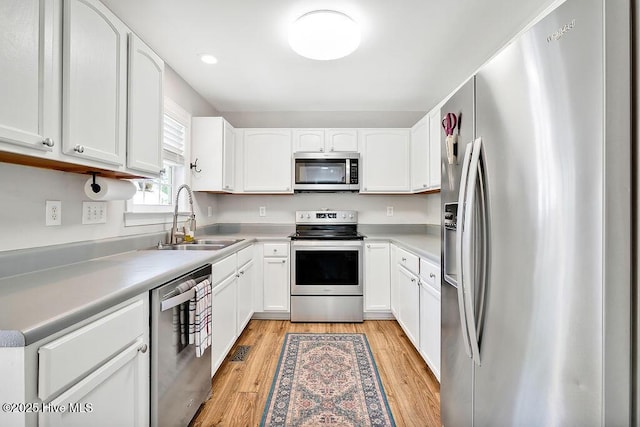 kitchen featuring stainless steel appliances, light wood finished floors, a sink, light countertops, and white cabinets