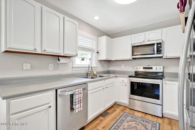 kitchen with light wood finished floors, white cabinets, appliances with stainless steel finishes, and a sink