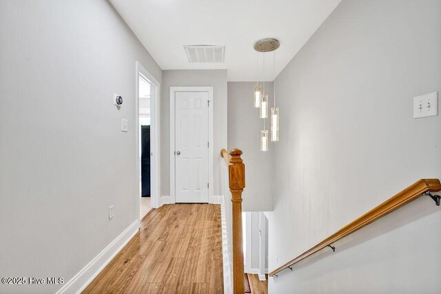 hallway featuring an upstairs landing, baseboards, visible vents, and light wood-style floors